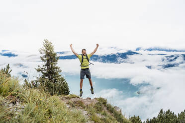 Glücklicher junger Mann mit erhobenen Armen bei einer Wanderung in den Bergen, Herzogstand, Bayern, Deutschland - DIGF08288