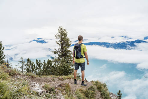 Junger Mann auf einer Wanderung in den Bergen mit Blick auf die Aussicht, Herzogstand, Bayern, Deutschland - DIGF08289