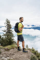 Junger Mann auf einer Wanderung in den Bergen mit Blick auf die Aussicht, Herzogstand, Bayern, Deutschland - DIGF08293