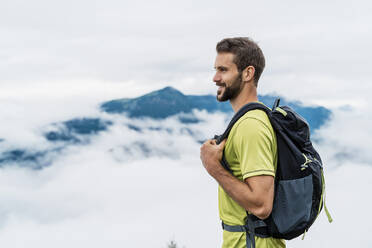 Lächelnder junger Mann bei einer Wanderung in den Bergen mit Blick auf die Aussicht, Herzogstand, Bayern, Deutschland - DIGF08295