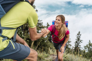 Young man helping girlfriend on a hiking trip in the mountains, Herzogstand, Bavaria, Germany - DIGF08296