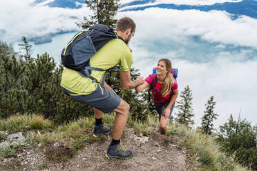 Young man helping girlfriend on a hiking trip in the mountains, Herzogstand, Bavaria, Germany - DIGF08297