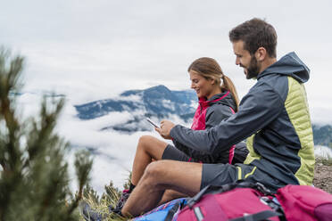 Junges Paar beim Wandern in den Bergen, Pause mit Handy, Herzogstand, Bayern, Deutschland - DIGF08307
