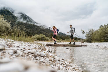 Young couple on a hiking trip crossing river on a log, Vorderriss, Bavaria, Germany - DIGF08328