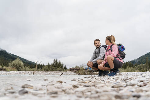 Junges Paar auf einer Wanderung, hockend am Flussufer, Vorderriss, Bayern, Deutschland - DIGF08334