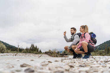 Junges Paar auf einer Wanderung, hockend am Flussufer, Vorderriss, Bayern, Deutschland - DIGF08335