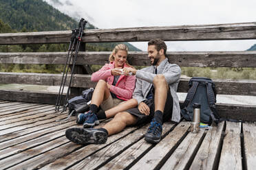 Junges Paar macht eine Pause auf einer Holzbrücke während einer Wanderung, Vorderriss, Bayern, Deutschland - DIGF08349