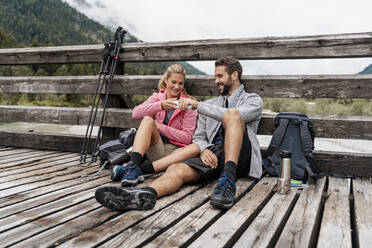 Young couple having a break on a wooden bridge during a hiking trip, Vorderriss, Bavaria, Germany - DIGF08349