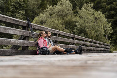 Junges Paar macht eine Pause auf einer Holzbrücke während einer Wanderung, Vorderriss, Bayern, Deutschland - DIGF08353