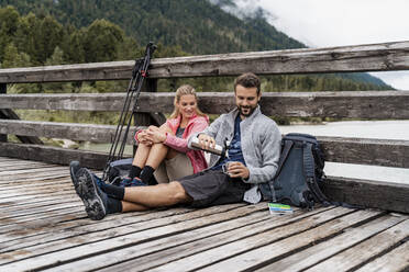 Junges Paar macht eine Pause auf einer Holzbrücke während einer Wanderung, Vorderriss, Bayern, Deutschland - DIGF08354