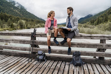 Junges Paar macht eine Pause auf einer Holzbrücke während einer Wanderung, Vorderriss, Bayern, Deutschland - DIGF08358