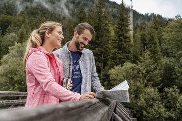 Glückliches junges Paar beim Wandern und Kartenlesen auf einer Holzbrücke, Vorderriss, Bayern, Deutschland - DIGF08364