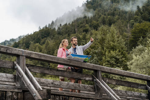 Junges Paar auf Wanderschaft mit Landkarte auf Holzbrücke, Vorderriss, Bayern, Deutschland - DIGF08365