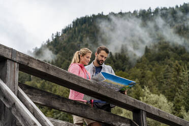 Young couple on a hiking trip reading map on wooden bridge, Vorderriss, Bavaria, Germany - DIGF08366