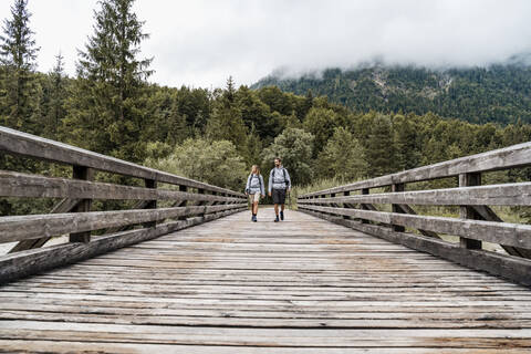 Young couple on a hiking trip walking on wooden bridge, Vorderriss, Bavaria, Germany stock photo