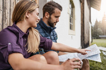 Young couple with map at a farmhouse during a hiking trip, Vorderriss, Bavaria, Germany - DIGF08383