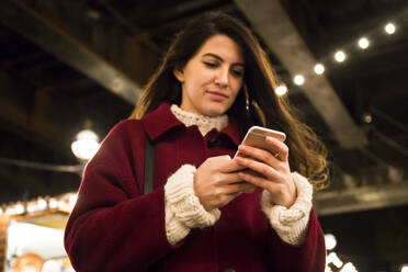 Portrait of young woman looking at cell phone on Christmas market - ABZF02569