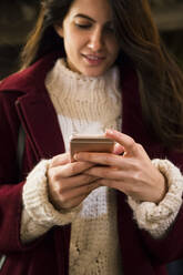 Young woman in red coat and knit pullover using smartphone, close-up - ABZF02571