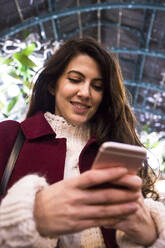 Porträt einer lächelnden jungen Frau, die auf ihr Mobiltelefon schaut - ABZF02582