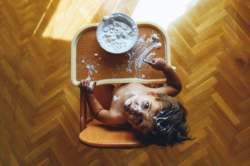 Kleiner Junge isst Joghurt zu Hause, sitzt im Hochstuhl, von oben - JCMF00189