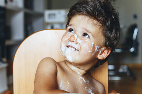 Kleiner Junge isst Joghurt zu Hause und schaut weg, lizenzfreies Stockfoto