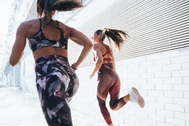 Rear view of two sporty young women running in the city - JCMF00197