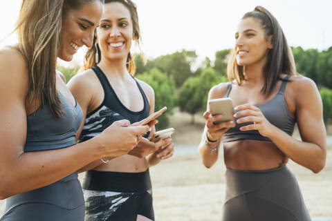 Drei glückliche Sportlerinnen nutzen Smartphones nach dem Training, lizenzfreies Stockfoto