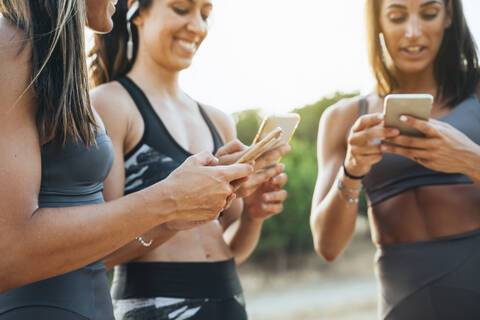 Drei Sportlerinnen nutzen Smartphones nach dem Training, lizenzfreies Stockfoto