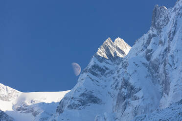 Blauer Himmel und Mond auf den schneebedeckten Graten der hohen Gipfel, Soglio, Bergell, Kanton Graubünden, Schweiz, Europa - RHPLF08812