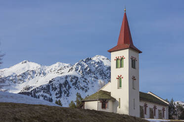 Die weiße Alpenkirche umrahmt von verschneiten Gipfeln, Maloja, Bergell, Kanton Graubünden, Engadin, Schweiz, Europa - RHPLF08817