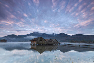 Rosa Wolken bei Sonnenuntergang und Holzhütten spiegeln sich im klaren Wasser des Kochelsees, Schlehdorf, Bayern, Deutschland, Europa - RHPLF08836