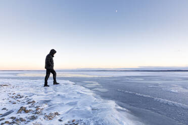 Mann, der bei Sonnenuntergang auf dem zugefrorenen Glan-See in Ostergotland, Schweden, spazieren geht - FOLF10936