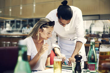 Kellner hilft einer Frau im Restaurant mit der Speisekarte - FOLF10959