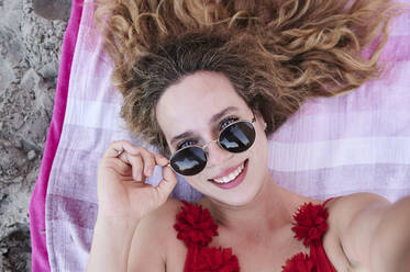 Self portrait of smiling young woman lying on towel on the beach - IGGF01311