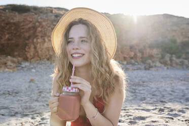 Glückliche junge Frau mit einem Smoothie am Strand - IGGF01312