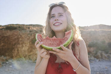 Glückliche junge Frau hält Wassermelonenscheibe am Strand - IGGF01314