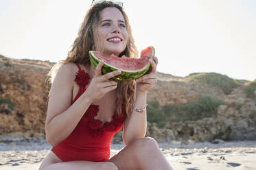 Glückliche junge Frau hält Wassermelonenscheibe am Strand - IGGF01316