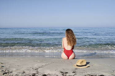 Rückansicht einer jungen Frau, die am Strand sitzt - IGGF01321