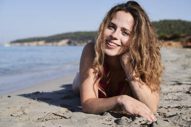 Portrait of happy young woman lying on the beach - IGGF01322