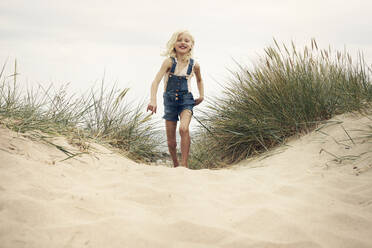 Girl wearing denim overalls walking on sand dune - FOLF11082