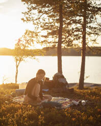 Junge Frau liest bei Sonnenuntergang am See Norra Bredsjon, Schweden - FOLF11134