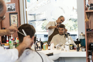Reflexion eines Friseurs, der einem jungen Mann die Haare schneidet, im Spiegel - FOLF11245