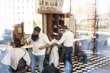 Blick durch das Fenster eines Friseurs, der einem Kunden die Haare schneidet - FOLF11246