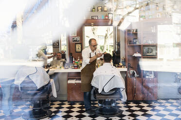 Blick durch das Fenster eines Friseurs, der einem Kunden die Haare schneidet - FOLF11248
