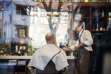 Friseur im Gespräch mit einem Kunden im Fenster des Friseursalons - FOLF11260