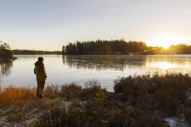 Mature woman standing next to Lake Skiren at sunset in Sweden - FOLF11317