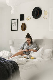 Junge Frau benutzt Smartphone im Bett - FOLF11358