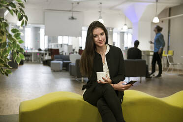 Young woman holding smart phone on office sofa - FOLF11381