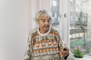 Senior woman using smart phone by window - FOLF11409