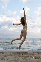 Junge Frau springt vor Freude am Strand - AFVF03890